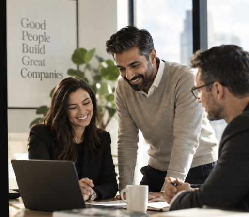 Three smiling professionals collaborating around a laptop in a warm office